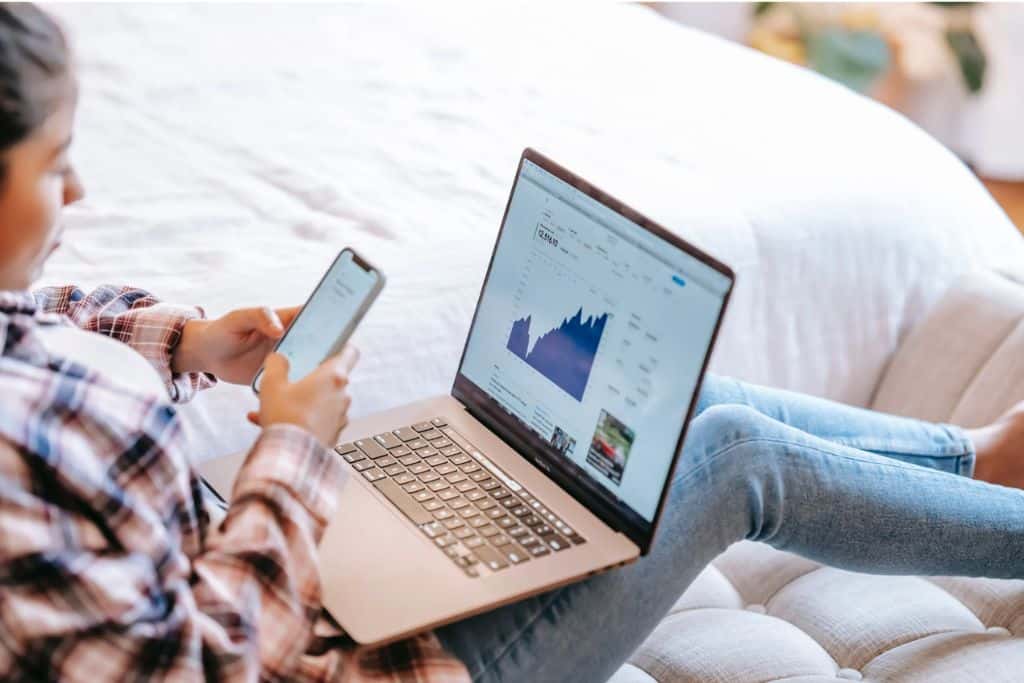 Woman checking the stock market trades she has invested in on her laptop and phone -TradeZella